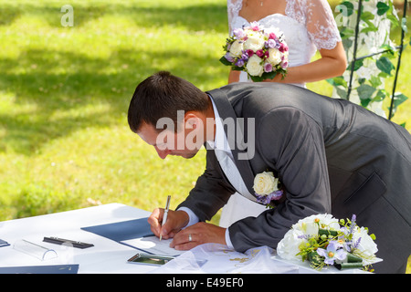 groom signing wedding certificate in park with bride in background