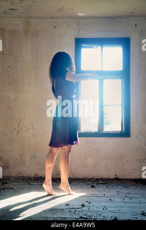 Young woman standing by the window reaching for the light Stock Photo
