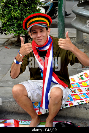 BANGKOK, THAILAND: Thai youth wearing colourful knit hat and a red, white, and blue knit neck scarf sitting on Silom Road Stock Photo