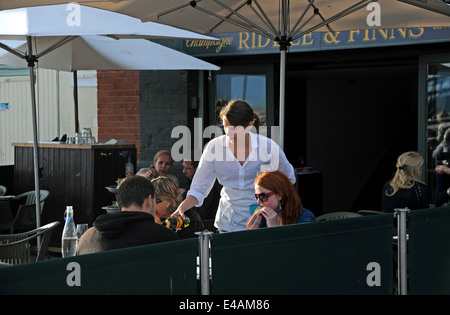 Waitress pouring wine to customers sitting outside at Riddle & Finns restaurant on Brighton seafront beach UK