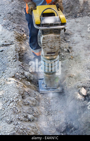 Worker uses compactor to firm soil at worksite Stock Photo