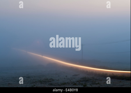 Valley fog with car light trails on rural road Stock Photo