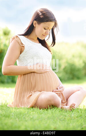 Attractive Pregnant Woman Sitting In Field Stock Photo