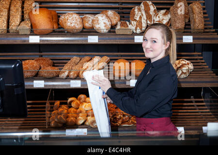 Female shop assistant in bakery packing bread into bag Stock Photo