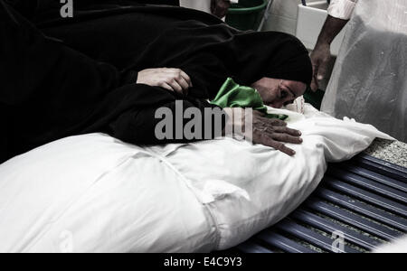 Sanabis, Bahrain. 6th July, 2014. Bahrain, Sanabis - martyr's mother in the last moments with her son, Thousands attend the funeral of Abdul Aziz al-Abbaar in the village of Sanabis west of the capital Manama, Abdulaziz was hit in his head by a tear gas canister and birds bullets shot on February 23rd when he was taking a part in clashes with riot police and died from wounds on April 18th, Al-Abbar's body was in the morgue for 76 days because his family refused to sign the death certificate which ministry of interior said his death was because of brain damage then they have change it to the Stock Photo