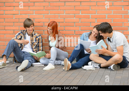 Group of students with books hanging out sitting against wall Stock Photo