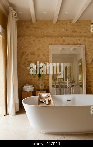 A Deep VAS 910 bath from Agape in bathroom with rough stone walls and large mirror Stock Photo