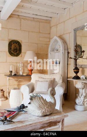 Swan sculpture on distressed wooden coffee table in sitting room with armchair and limestone walls Stock Photo