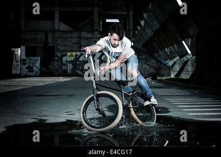 BMX biker performing a stunt on a puddle Stock Photo