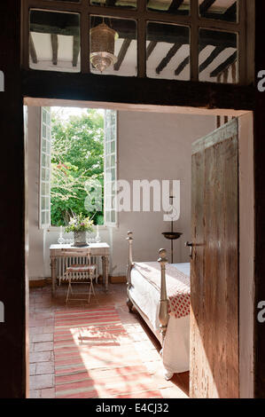 View through open doorway to bedroom with terracotta tiled floor, red striped kilim and writing desk by crittall windows Stock Photo