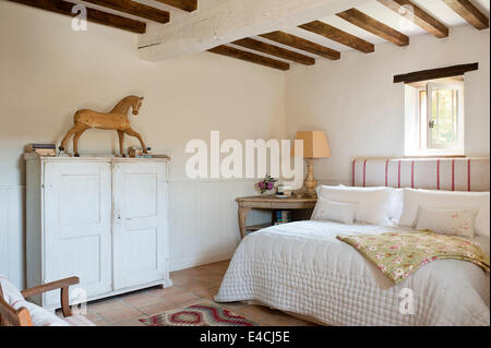 Old wooden horse model on top of a distressed white cupboard in bedroom with ceiling beams and quilt Stock Photo