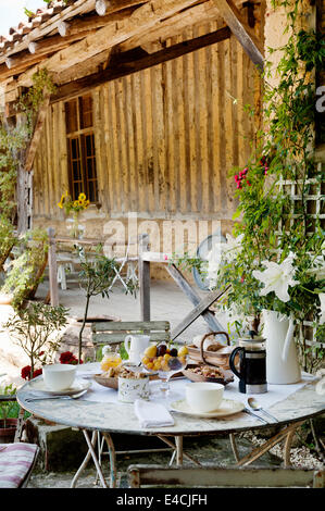 Breakfast laid on round table with folding bistro chairs in courtyard by old barn