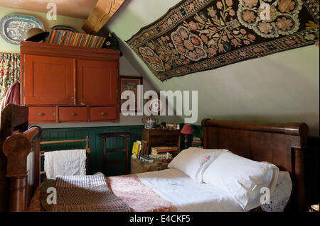 An Uzbekistani textile hangs above a French empire bed in cottage bedroom with tweed patchwork quilt and monogrammed linen Stock Photo