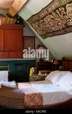 An Uzbeki Suzani textile hangs above a French empire bed in cottage bedroom with tweed patchwork quilt and monogrammed linen Stock Photo