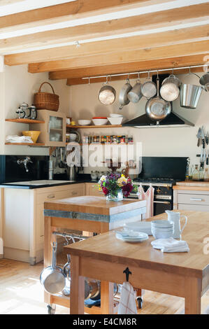 Pots and pans hang from a rack in a rustic kitchen with wooden ceiling beams and butchers block Stock Photo