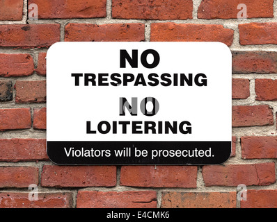 A bold no trespassing no loitering sign attached to an old brick wall. Stock Photo