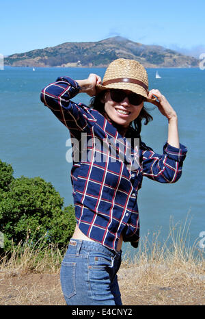 pretty woman hangs onto hat on windy bluff overlooking San Francisco bay Stock Photo