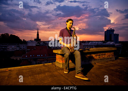 Man playing the saxophone on rooftop at sunset, Osijek, Croatia Stock Photo