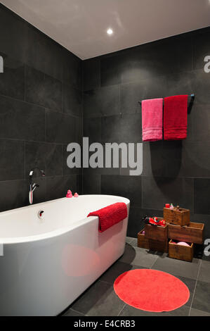 Bright red and pink towels in bathroom with slate tiling and Catalano bath Stock Photo