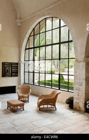 Stone floored gallery style space with large arched window and wicker furniture Stock Photo
