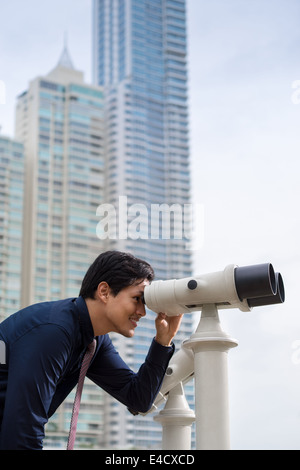 Portrait of young chinese business man standing in Panama City and looking through binoculars. Concept of forecasting, career Stock Photo