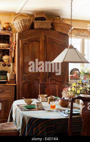 Wicker baskers sit on top of a large armoire in kitchen with georgian dining table and triped tablecloth Stock Photo