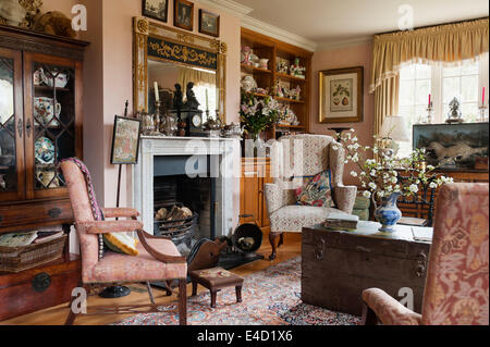 Wing back armchair by fireplace in drawing room with assorted china collections and ornate French gilt mirror Stock Photo