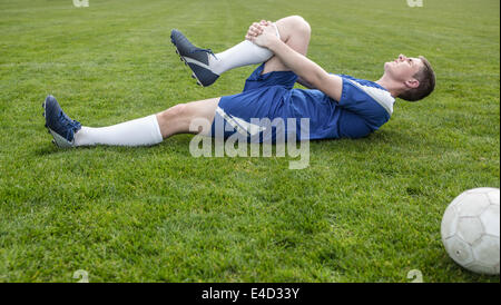 Football player in blue lying injured on the pitch Stock Photo