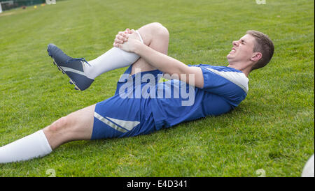 Football player in blue lying injured on the pitch Stock Photo
