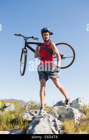 Fit cyclist carrying his bike on rocky terrain Stock Photo