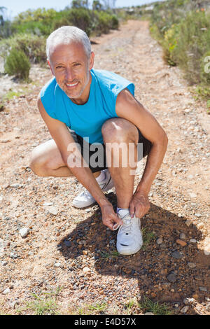 Smiling jogger tying his shoelace on mountain trail Stock Photo