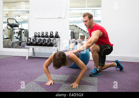 Personal trainer with client doing push up on exercise ball Stock Photo