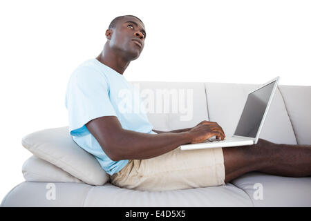 Thoughtful man sitting on couch using laptop Stock Photo