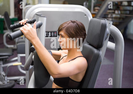 Happy brunette using weights machine for arms Stock Photo