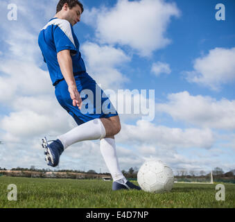 Football player in blue kicking the ball on pitch Stock Photo