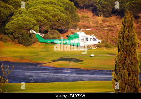 Bell 412 registration EC-IPM collecting water for fire fighting from a golf club lake, Cabopino Golf, Costa del Sol, Spain. Stock Photo