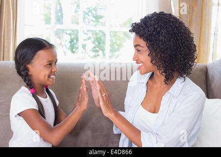 Pretty mother playing clapping game with daughter on couch Stock Photo