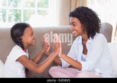 Pretty mother playing clapping game with daughter on couch Stock Photo