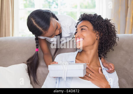 Pretty mother sitting on couch with daughter offering a gift Stock Photo