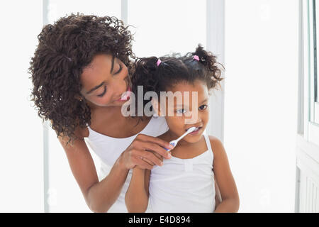 Pretty mother helping her daughter brush her teeth Stock Photo