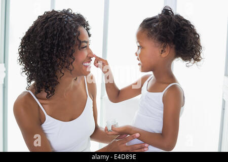 Cute daughter putting face cream on mothers nose Stock Photo
