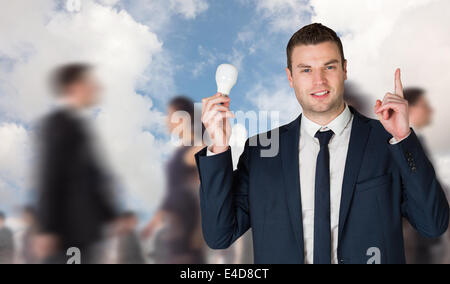 Composite image of businessman holding light bulb and pointing Stock Photo