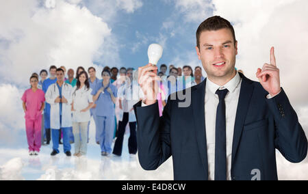 Composite image of businessman holding light bulb and pointing Stock Photo