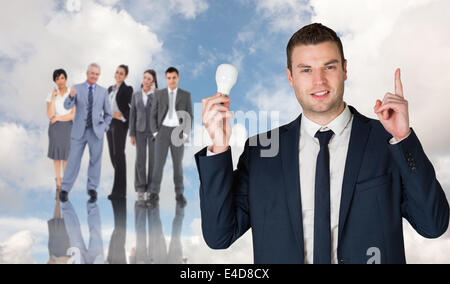 Composite image of businessman holding light bulb and pointing Stock Photo