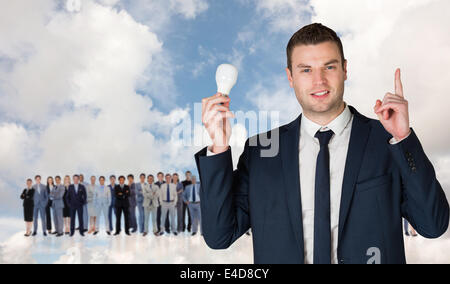 Composite image of businessman holding light bulb and pointing Stock Photo