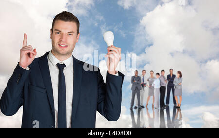 Composite image of businessman holding light bulb and pointing Stock Photo