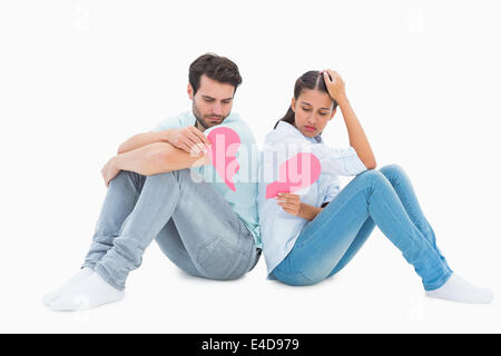 Sad couple sitting holding two halves of broken heart Stock Photo