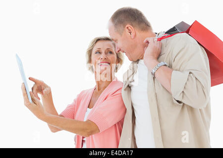 Smiling older couple holding shopping bags looking at tablet pc Stock Photo