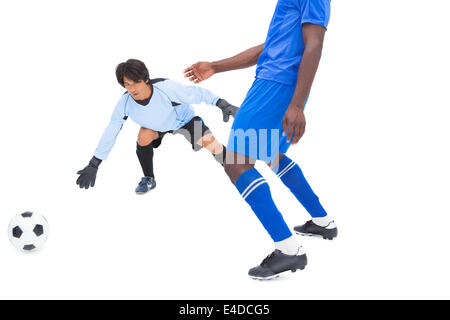 Football player in blue striking at keeper Stock Photo