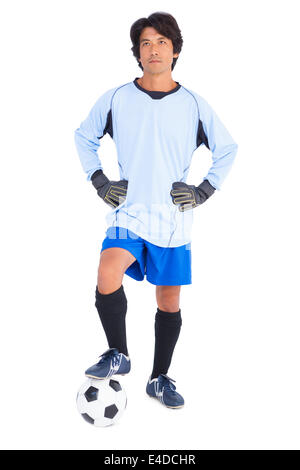 Goalkeeper in blue holding ball with foot Stock Photo